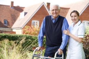 caregiver helps elderly man to walk in garden using walking frame